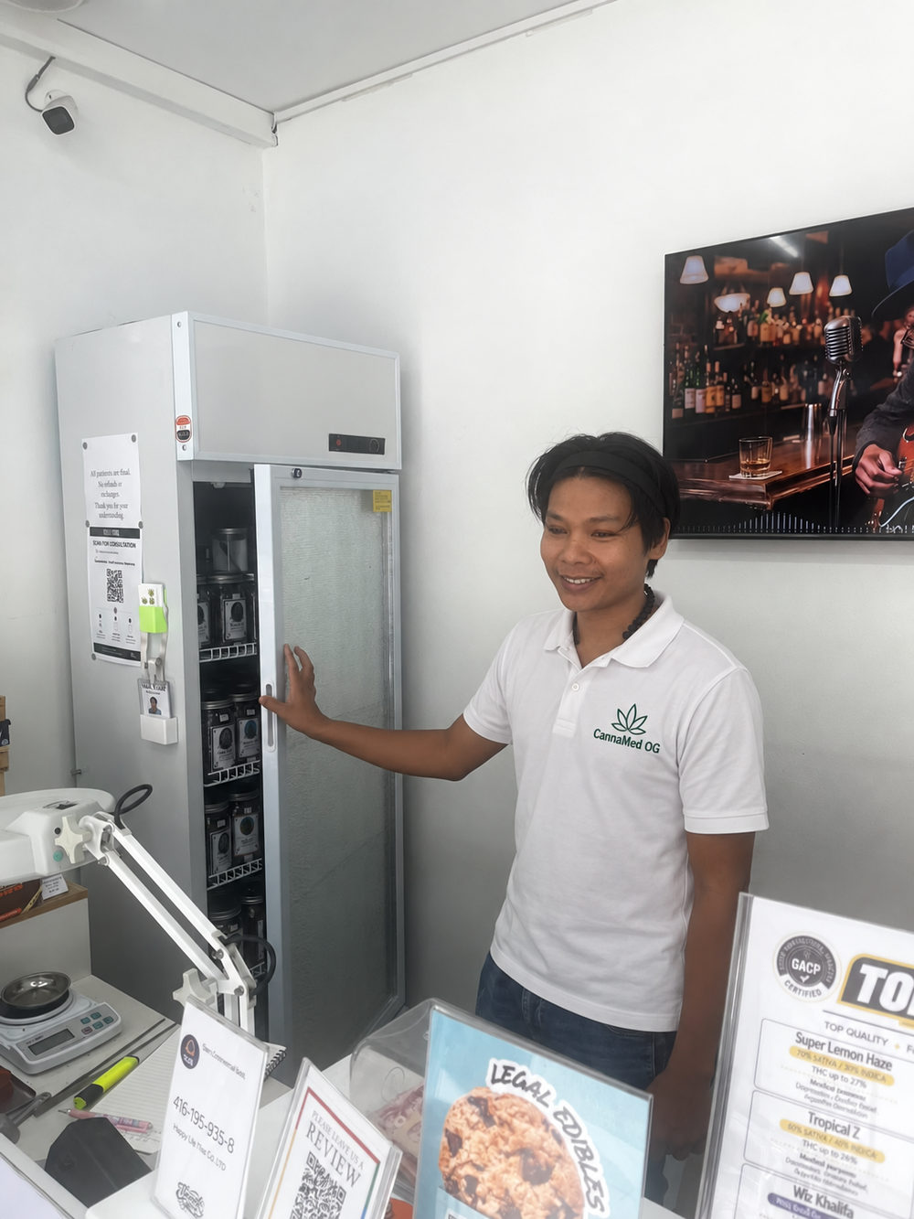 Thar Thar, lead budtender at CannaMed OG, beside the flower refrigerator in the Lamai dispensary